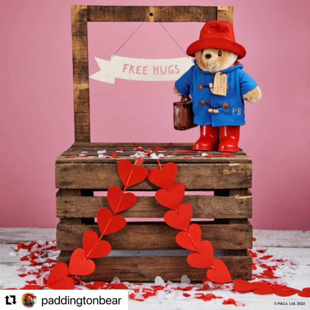 Photograph of Paddington Bear teddy standing on a wooden crate draped with hearts.